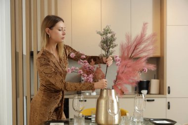 Yemek masasında çiçekli vazo düzenleyen kadın. Ev hanımı evdeki rahatlıkla ilgileniyor. İç dekorasyon, ev ve ev dekorasyonu kavramı.