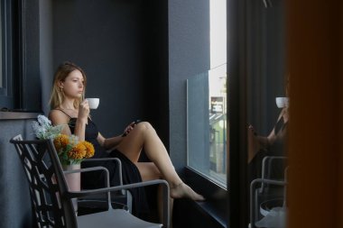 Balkonda oturup kahve içen şık bir kadının portresi.