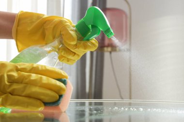 Lastik eldivenli bir kadın kahve masasını spreyle temizliyor. Spreyleme ve cam silme masası.