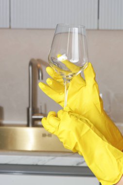 Sarı lastik eldivenli biri mutfaktaki şarap kadehinin temizliğini kontrol ediyor..