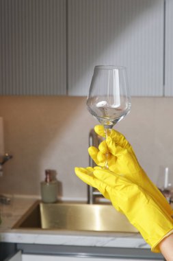 Sarı lastik eldivenli biri mutfaktaki şarap kadehinin temizliğini kontrol ediyor..