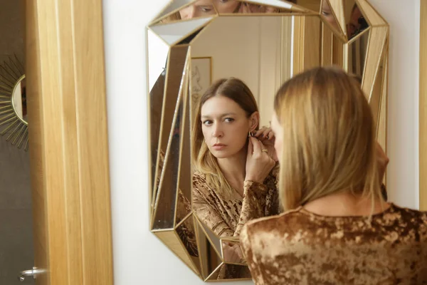エレガントなファッショナブルな女性が鏡を見つめ イヤリングを着用 — ストック写真
