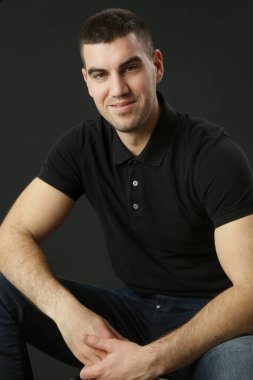 Siyah arka planda siyah polo tişörtlü genç adamın stüdyo portresi.