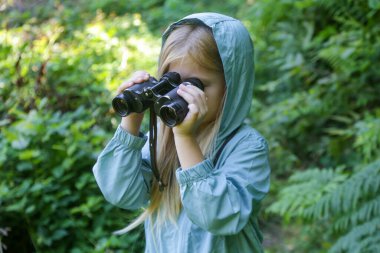 Dürbünle doğayı keşfeden sevimli küçük bir kız. Çocuk dışarıda oynuyor. Çocuklar seyahat, macera ve kuş izleme konsepti.