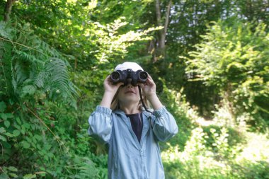 Dürbünle doğayı keşfeden sevimli küçük bir kız. Çocuk dışarıda oynuyor. Çocuklar seyahat, macera ve kuş izleme konsepti.