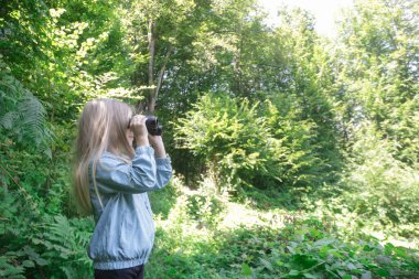 Dürbünle doğayı keşfeden sevimli küçük bir kız. Çocuk dışarıda oynuyor. Çocuklar seyahat, macera ve kuş izleme konsepti.