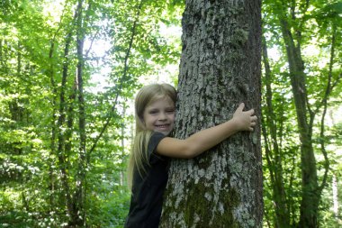 Sevimli küçük kız sarılıyor. Ağaçlara sarılmak ve dokunmak çocuklar için zengin duyusal deneyim sağlar, stresi azaltır, bağışıklığı artırır, tansiyonu düşürür, travmayı hızlandırır.