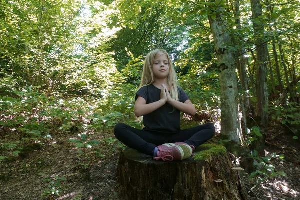 Little girl in lotus position sitting on the tree stump. Forest meditation concept. Peace, mindfulness and relaxation in nature.