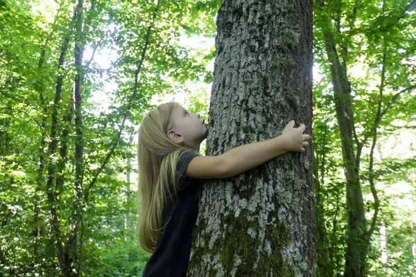 Cute little girl hugging tree. Hugging and touching trees provide rich sensory experience for children, reduce stress, improve immunity, lower blood pressure, accelerate recovery from trauma
