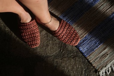 Çizgili el yapımı yün halıda el yapımı rafya katırları üzerinde duran kadın. Etik açıdan sürdürülebilir bir çift terlik. Sorumlu kaynak ayakkabılar ve çevre dostu malzemeler..