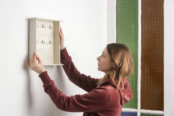 Young woman is hanging wooden key holder on the wall, moving into the new apartment or home decor concept