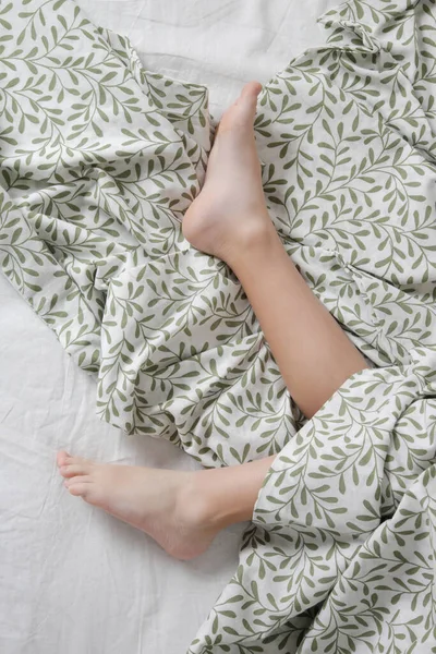 Child feet under cotton bedcover under soft morning light