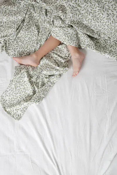 Child feet under cotton bedcover under soft morning light