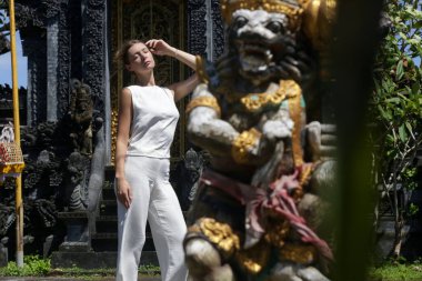 Endonezya, Bali 'deki Hindu tapınağının önünde poz veren beyaz keten elbiseli beyaz kadın.