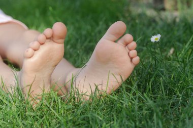 Yeşil çimenlerin üzerinde çocuk ayakları, çayır üzerinde yalın ayak küçük kız, kırsal yaşam tarzı, topraklama ve doğayla bağ kurma kavramı