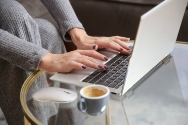 Oturma odasındaki sehpanın üstünde dizüstü bilgisayarda yazan kadın elleri.