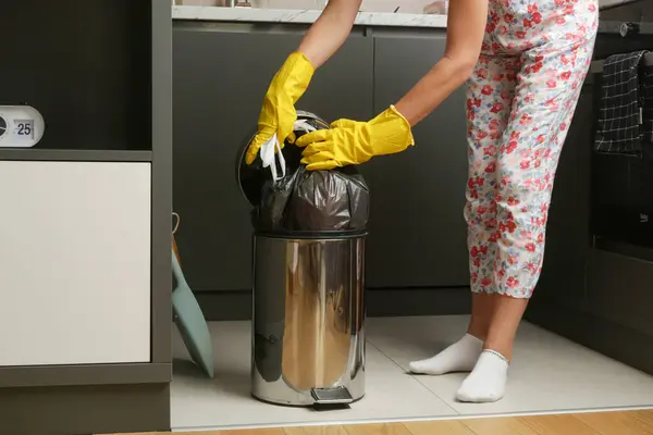 Housewife throwing away garbage, taking of plastic garbage bag from the trash bin in the apartment