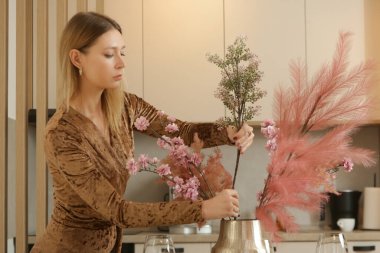 Yemek masasında çiçekli vazo düzenleyen kadın. Ev hanımı evdeki rahatlıkla ilgileniyor. İç dekorasyon, ev ve ev dekorasyonu kavramı.