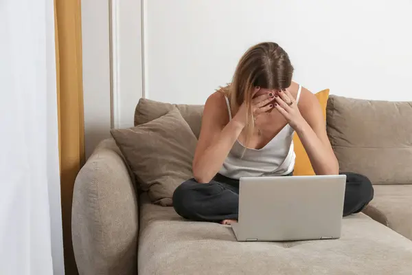 Portrait of young worried, depressed woman working from home. Writer, blogger, freelancer or student covering face with hands in front of laptop, Woman under the pressure, receiving bad news.