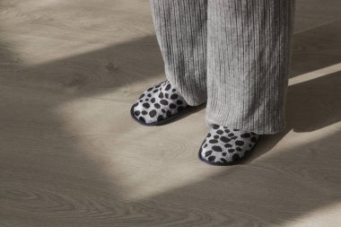 Gri ev terlikleri giyen ve apartmanın ahşap zemininde duran bir kadın.