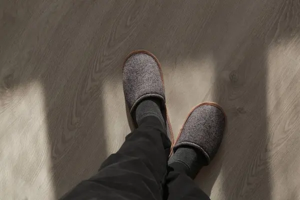 Man wearing grey home slippers and standing on hardwood flooring in apartment