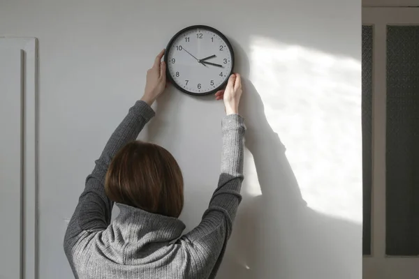 Young woman hanging clock on the wall, back view