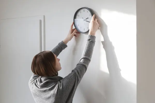 Young woman hanging clock on the wall, back view