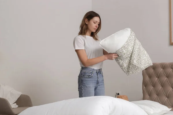 Woman changing bed linens at home in her bedroom, cozy domestic lifestyle, housewife cleaning, tidying up bedroom, housework concept.