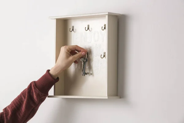 Young woman is hanging keys on the key holder on the wall, domestic living concept