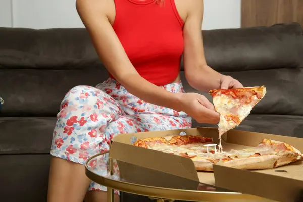 Woman eating take-out pizza from box while resting on sofa at home