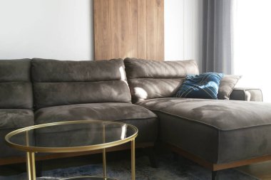 Büyük pencerenin yanında mavi yastıklı, gri rahat kanepe.