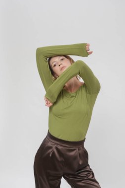 Stüdyo fotoğrafları, rahat basit kıyafetler giyen genç bir kadın model, yeşil yapışkan gömlek ve kahverengi pantolon.