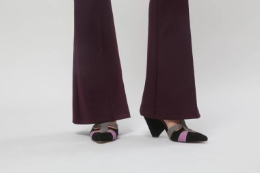 Stüdyo fotoğrafları. Genç bir manken. Alevli mor pantolon ve üçgen topuklu sandalet giyiyor.