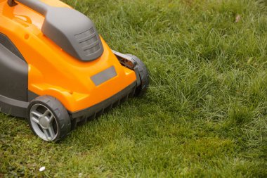 Bahçedeki yeşil çimlerin üzerinde turuncu çim biçme makinesi
