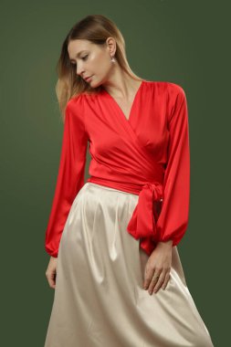 Stüdyo fotoğrafları. Sade bej renkli midi etekli ipek kırmızı bluz giyen genç bir kadın model. Rahat ve zarif bir moda..