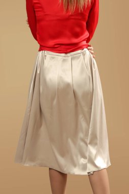 Stüdyo fotoğrafları. Sade bej renkli midi etekli ipek kırmızı bluz giyen genç bir kadın model. Rahat ve zarif bir moda..
