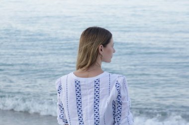 Beyaz mavi elbiseli orta yaşlı kadın boş kumsalda eğleniyor.