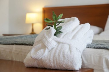 Otel odasındaki yatağın üzerinde zeytin dalı olan beyaz pamuklu bornoz. Turizm, oteller, konukseverlik endüstrisi