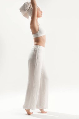 Beyaz pamuklu sutyen, pantolon ve havluyla stüdyoda poz veren güzel bir kadın. Pozitif ve mutlu bir bayanın sabah keyfi. Refah ve kendine bakım kavramı.