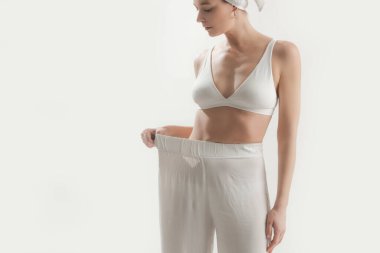 Diyet sonrası büyük pantolon giyen beyaz tenli genç bir kadının stüdyo fotoğrafı.