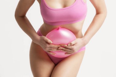 Young woman holding balloon as a sign of an stomach inflation, bloating and menstrual cramps concept clipart