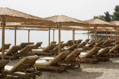 Boş plaj, saman şemsiyeler ve tahta güneşlikler.