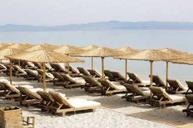 Boş plaj, saman şemsiyeler ve tahta güneşlikler.