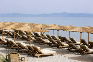 Boş plaj, saman şemsiyeler ve tahta güneşlikler.