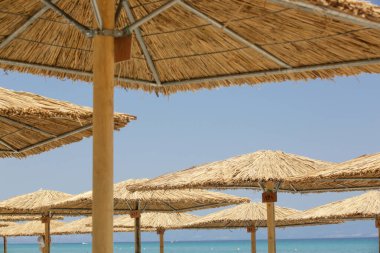 Açık mavi gökyüzüne karşı saman şemsiyeli tropik sahil manzarası