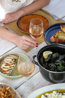 Genç bir kadın Akdeniz lokantasında yemek yiyor. Masada bir bardak gül ve çeşitli tabaklar var..
