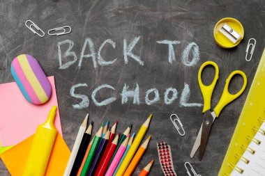 Siyah karatahta arka planında çeşitli ofis ve okul malzemeleriyle okul konseptine geri dönelim..