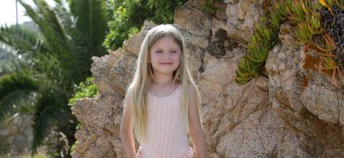 Pembe mayo giymiş şirin sarışın bir kızın samimi portresi kayalık sahilde eğleniyor.