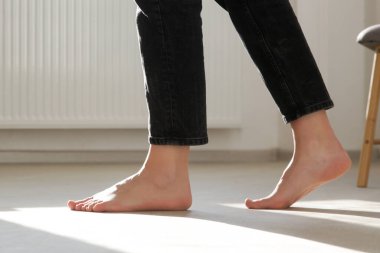 Ahşap zeminde çıplak ayaklı kadın. Dairenin alt katındaki ısıtma konsepti.