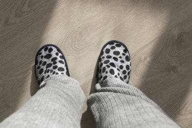 Gri ev terlikleri giyen ve apartmanın ahşap zemininde duran bir kadın.